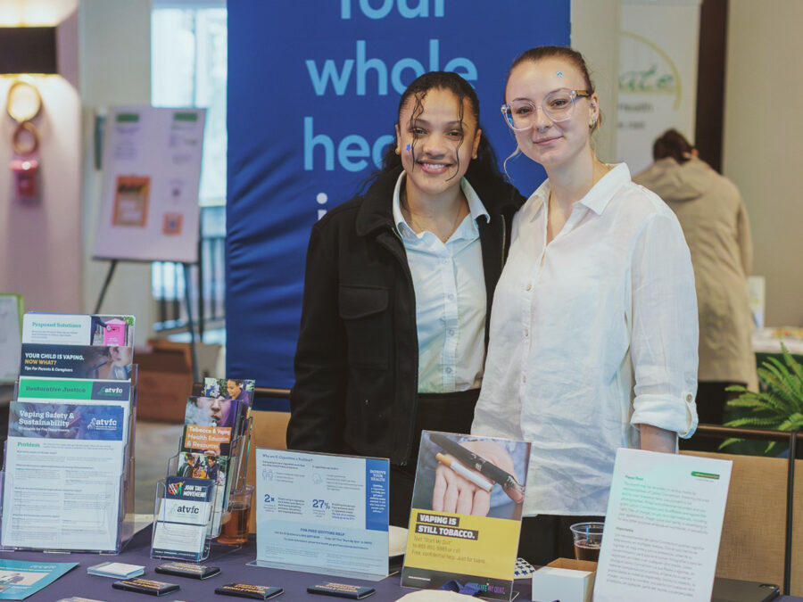 Two team members posing for the camera as they stand behind table with ATVFC collateral